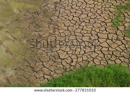 Top view background texture of dry, cracked earth with grass growing in patches.