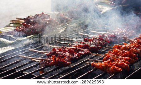 Grilled chicken skewers on a row of steel bars placed on hot coals with much smoke.