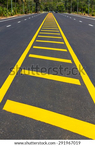 View shaped yellow stripes that divide the paved road that leads to a small hill.