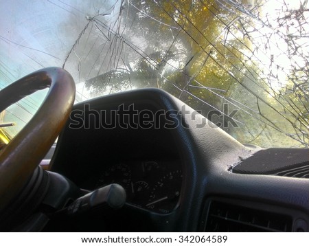 Inside the car, sunny, with windshield cracks due to accident damage.