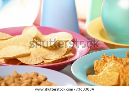 Children\'s party table with potato chips and nachos in plastic plates with colored balloons in the background