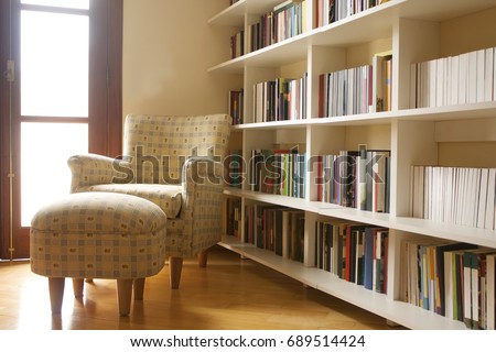 Home library with arm chair. Clean and modern decoration. Light coming from the window.
