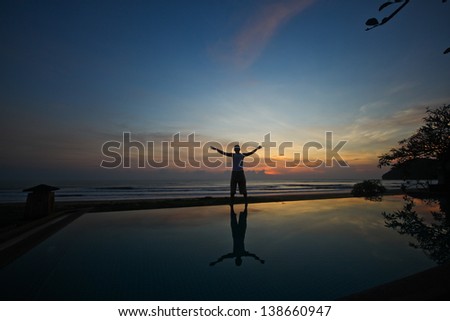 Standing with his arms outstretched before watching the beautiful sunrise dawn seaside.