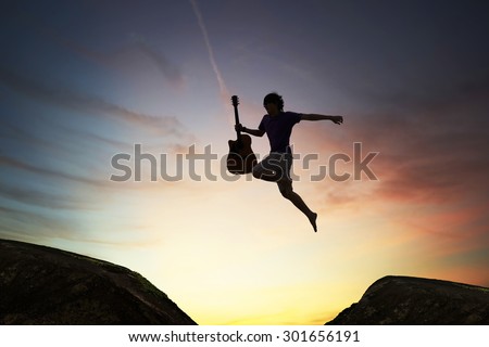 silhouette of brave guy holding the guitar jumping  through the gap,?inspiration and success concept.