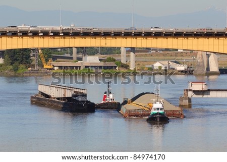 Two tugboats maneuver a barge full of sand past a rail bridge and up the north arm of the Fraser River near the Oak Street Bridge. Vancouver, British Columbia, Canada.