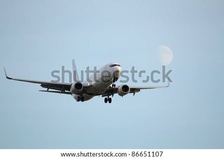 A jet airplane on approach for landing. Landing gear down, and the moon off one wing.