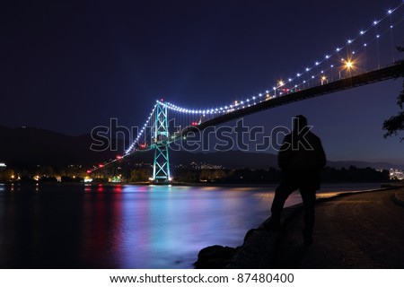 The Lions Gate bridge at twilight. A pedestrian takes in the view from the seawall which surrounds Stanley Park. Vancouver, British Columbia, Canada.