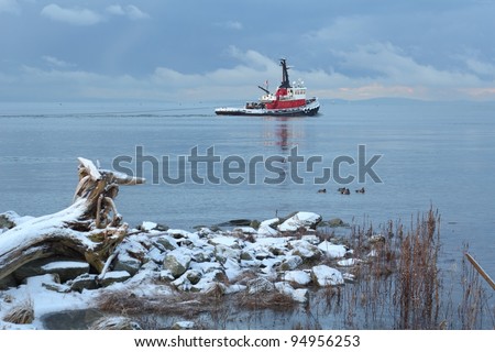 A tug boat on the Fraser River heads into Georgia Strait on a snowy, winter morning as a storm builds in the background. Near Vancouver. British Columbia, Canada.