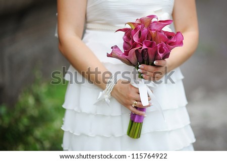 Bride holding wedding bouquet of calla lilies against dress