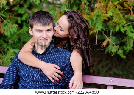 lovers on a bench in the park, woman bites the guy behind the ear