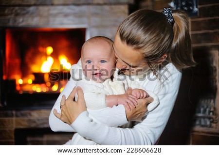 mother kisses daughter at the burning fireplace.