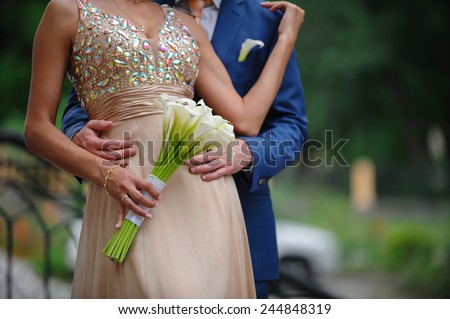 groom hugging woman at a wedding bouquet of white calla lilies.