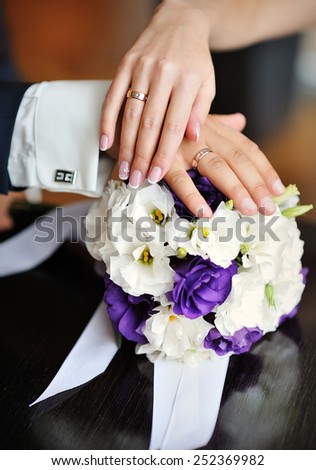 hands of the bride and groom with wedding rings on a background of the bouquet.