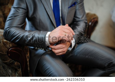 man in a suit sitting in a chair and puts cufflinks.