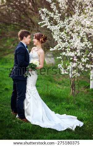 Bride and groom stand near a flowering tree in spring garden.