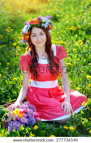Beautiful woman in red dress sitting on the grass with a branch of lilac.