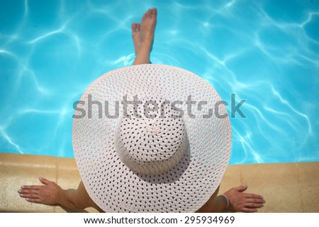 beautiful woman in a white hat sitting on the edge of the pool