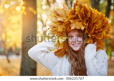 happy woman in a wreath of yellow leaves walking in autumn park