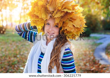 happy woman in a wreath of yellow leaves walking in autumn park