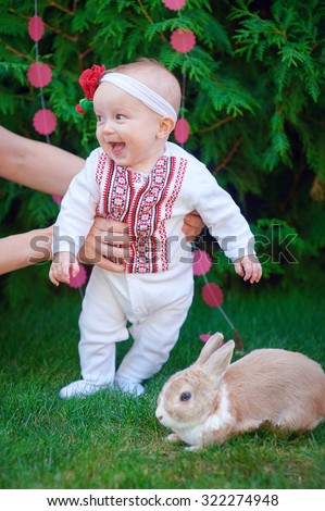 Cute funny happy baby with rabbit making his first steps on a green grass in a sunny summer garden