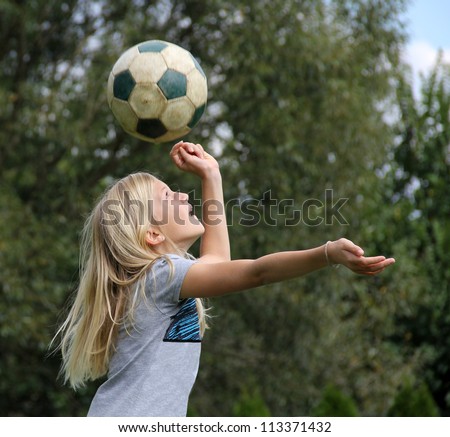 11-year old blond girl playing with a football, reaching to head the ball