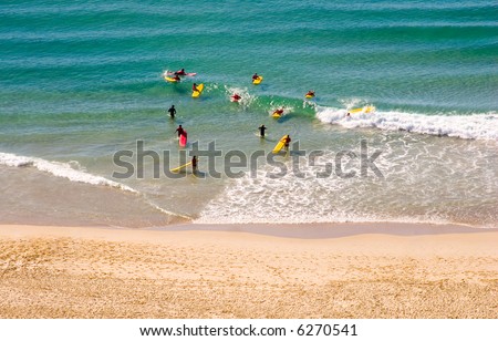Young people learning to surf at a surf school, teachers in the ocean water with them.