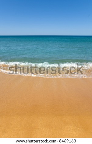 absolute perfect beach with golden sand. a gentle wave washes onto shore. The shallow water is turquoise aqua to the deep blue of the ocean. Perfect Blue Sky and beach for copyspace
