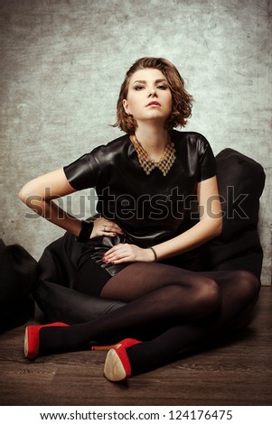 beautiful model posing in the studio in a leather dress and red shoes