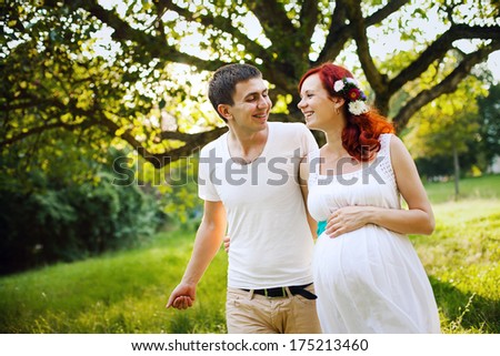Young married couple walking in the park. Young beautiful pregnant woman hugging her husband.