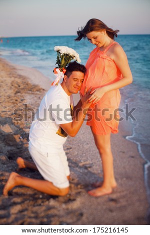 Happy young couple walking along the beach. Pregnant woman hugging her husband