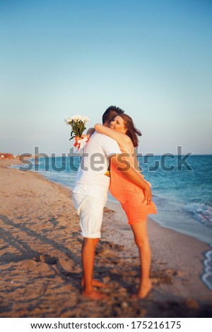 Happy young couple walking along the beach. Pregnant woman hugging her husband