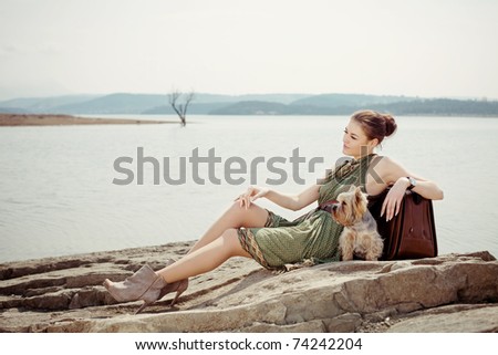 Fashion shot of a beautiful, professional model on the lake with a suitcase and a dog (Yorkshire terrier)