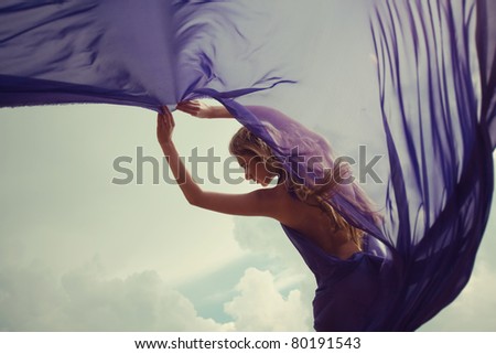 Beautiful blonde girl in a blue dress standing in the wind against the sky