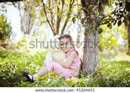 Little girl plays with a teddy bear in the apple garden