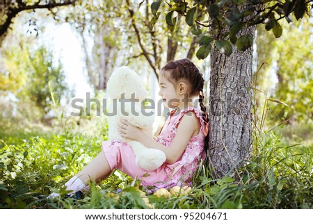 Little girl plays with a teddy bear in the garden