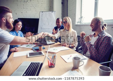 New business partners. Young modern colleagues in smart casual wear shaking hands and smiling while sitting in the creative office