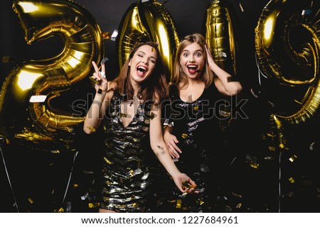 Beautiful Women Celebrating New Year. Happy Gorgeous Girls In Stylish Sexy Party Dresses Holding Gold 2019 Balloons, Having Fun At New Year\'s Eve Party. Holiday Celebration