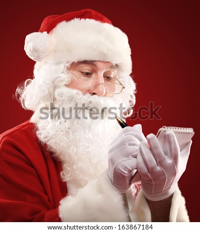 Christmas portrait of Santa Claus writing a list isolated over a red background
