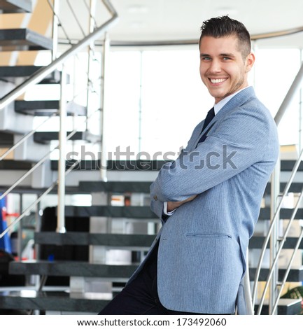 Portrait of positive business man standing on stairs of modern office