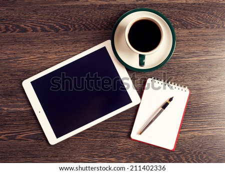 Digital tablet computer with note paper and cup of coffee on old wooden desk. Simple workspace or coffee break with web surfing.