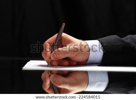 Man signing a document or writing correspondence with a close up view of his hand with the pen and sheet of notepaper on a desk top