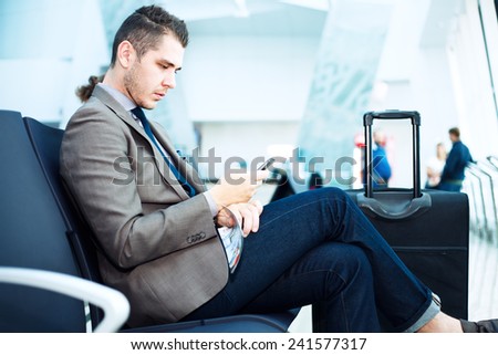 Businessman at airport with smartphone and suitcase checking emails before boarding