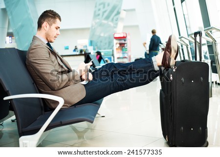 Businessman at airport with smartphone and suitcase checking emails before boarding