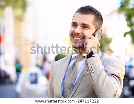 Handsome and confident businessman or manager talking on his business cell phone walking in front of modern architecture