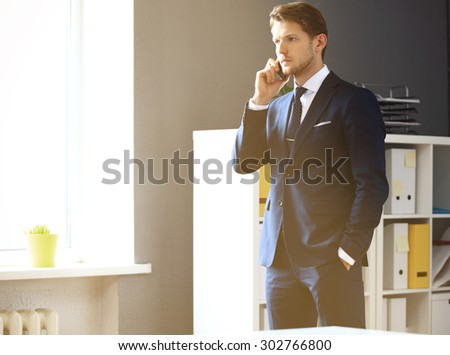 Handsome businessman in suit speaking on the phone in office