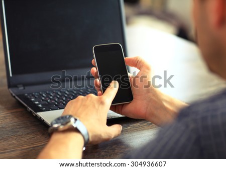 Silhouette of cropped shot of a young man working from home using smart phone and notebook computer, man\'s hands using smart phone in interior, man at his workplace using technology, flare light