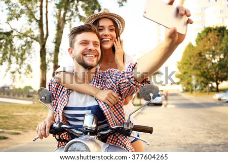 Happy couple on scooter making selfie photo on smartphone outdoors