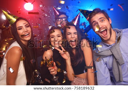 Friends making big party in the night. Four people throwing confetti and drinking champagne
