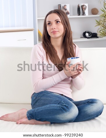 Pretty happy relaxed young lady sitting with coffee cup on couch