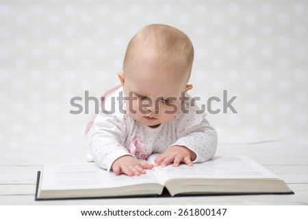 Baby girl lying on the belly reading a book